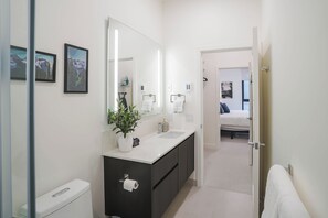Ein modernes Badezimmer mit einem weißen Waschbecken, dunklen Schränken, einem großen Spiegel und gerahmten Bildern an der Wand.