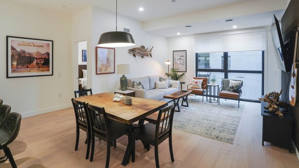 A modern living room with a wooden dining table, comfortable seating, and a large window offering a view. - Mackenzie Mountain Hop (Revelstoke)