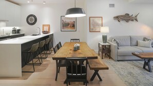 A modern kitchen with a central island, a dining area with a wooden table and chairs, and a living area with a sofa and a coffee table. - Mackenzie Mountain Hop (Revelstoke)