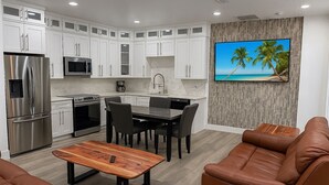 Eine moderne Küche mit weißen Schränken, Edelstahlgeräten, einem Essbereich mit Holztisch und einem braunen Ledersofa.