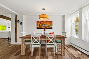 Ein Essbereich mit Holztisch, weißen Stühlen, einer Pendelleuchte und einem Gemälde von Herbstlaub.