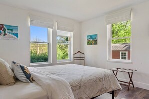 A bedroom with a bed, two windows, a wooden chair, and two wall-mounted paintings. - Country Chic 3BR Retreat Near All Star Village (Treadwell)