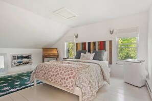 Ein Schlafzimmer mit Bett, Schminktisch, Heizkörper und einem Fenster mit Blick auf Grünflächen.