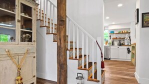 Eine Treppe mit Holzboden und weißen Geländern, die zu einem Küchenbereich mit weißen Schränken und einer Holzarbeitsplatte führt.