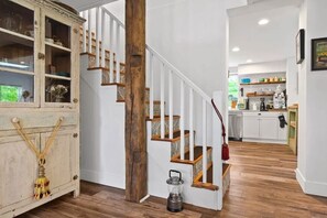 Eine Treppe mit Holzboden und weißen Geländern, die zu einem Küchenbereich mit weißen Schränken und einer Holzarbeitsplatte führt.