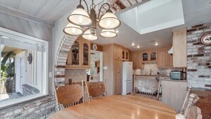 A dining area with a wooden table and chairs, a brick wall, and a kitchen with wooden cabinets and a refrigerator. - Trentadue Winery Farmstay with Pool and Wine Tastings Included (Geyserville)