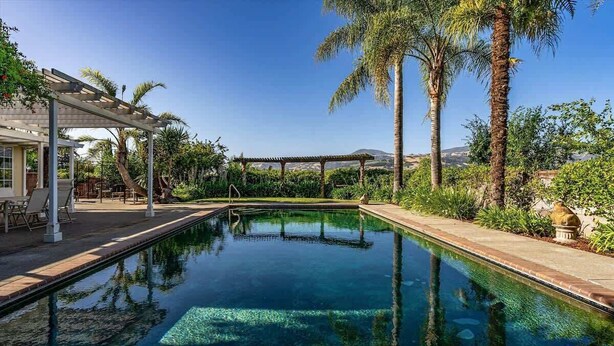 A clear swimming pool with a 'KEEP OFF' sign, surrounded by palm trees and a pergola. - Trentadue Winery Farmstay with Pool and Wine Tastings Included (Geyserville)