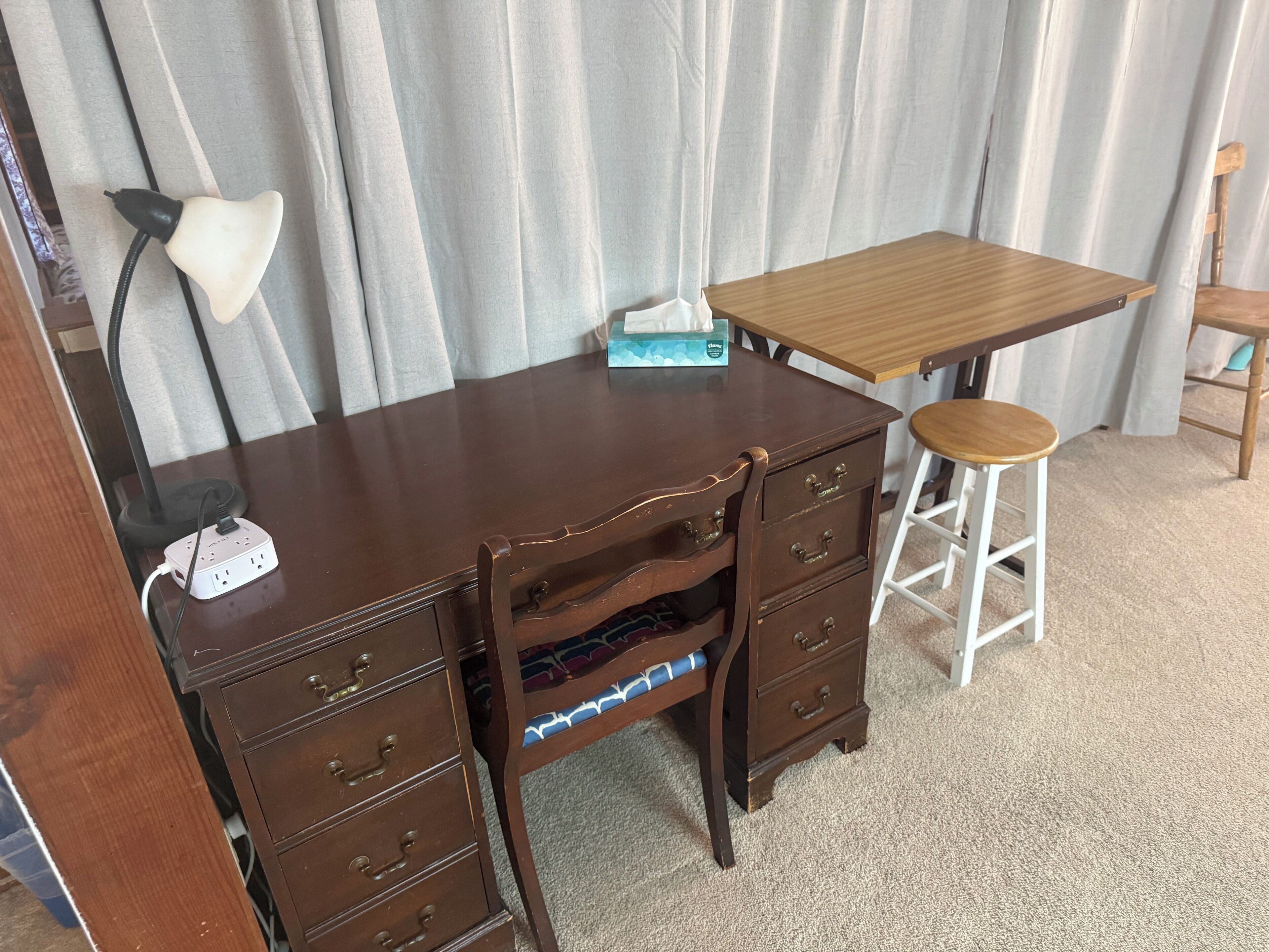 A wooden desk with drawers, a lamp, and a box of tissues.