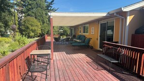 A covered deck with outdoor furniture, a wooden railing, and a view of the surrounding greenery. - Spacious house in marvelous Healdsburg close to town (Healdsburg)