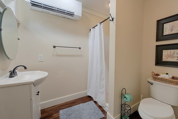 Une salle de bain avec un lavabo blanc, un miroir, un rideau de douche, des toilettes et un tableau encadré au mur.