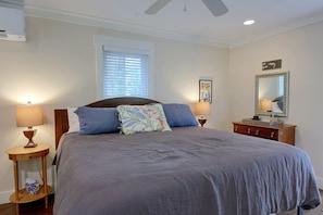 A bedroom with a bed, two bedside tables, a window with blinds, a ceiling fan, and a wall-mounted mirror. - Steps to Riverfront: Dtwn Bluffton Studio! (Bluffton)