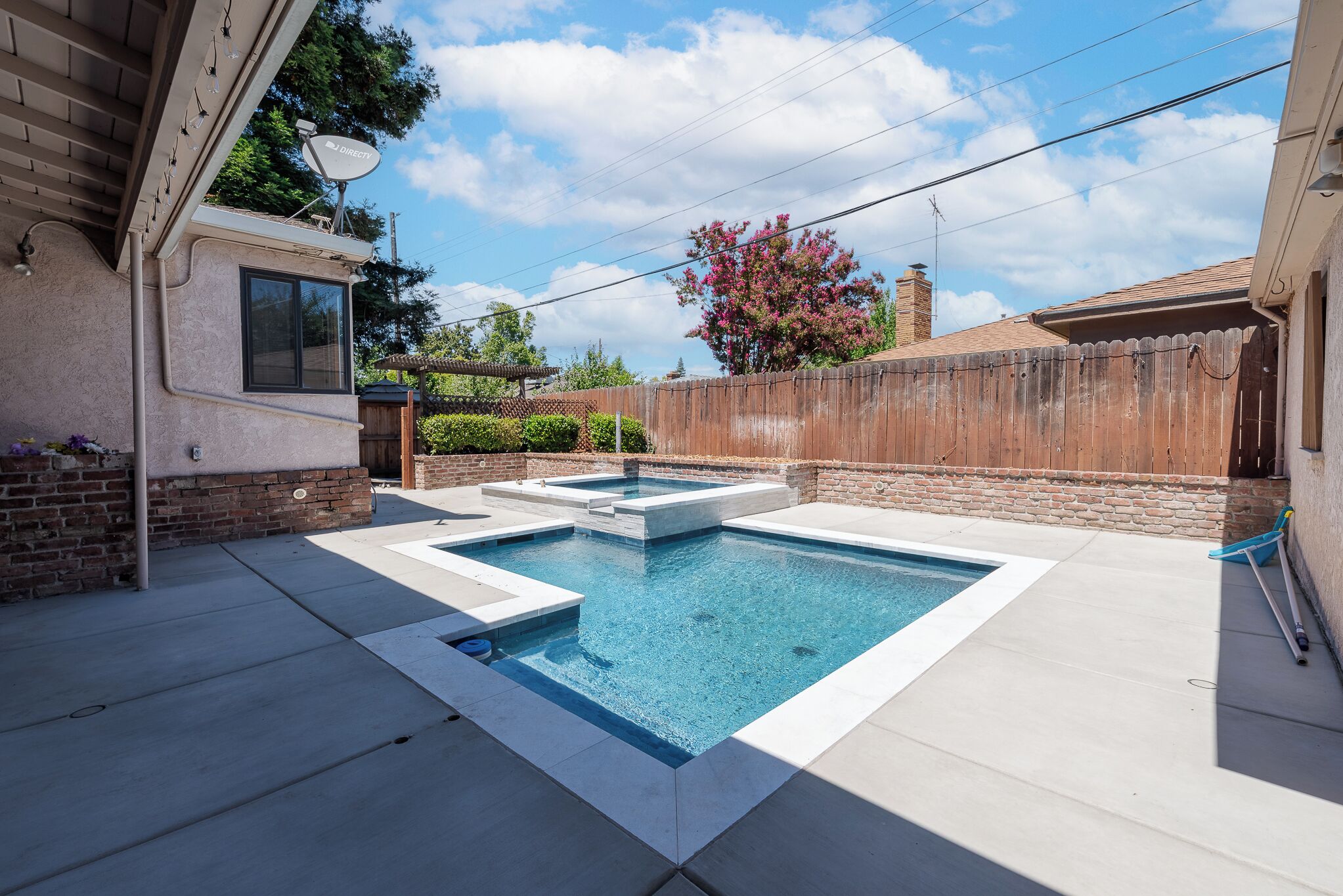 A rectangular swimming pool with a small hot tub, surrounded by a concrete deck.