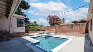 Une piscine rectangulaire avec un petit jacuzzi, le tout entouré d’une terrasse en béton.