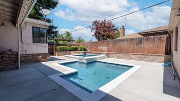 A rectangular swimming pool with a small hot tub, surrounded by a concrete deck.