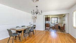 Un espace repas avec une table et des chaises en bois, un lustre, et une vue sur la cuisine et le salon.