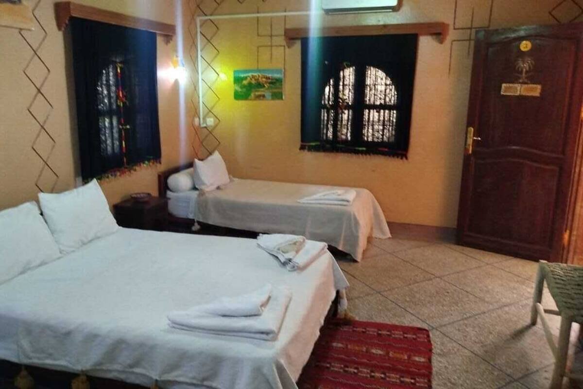 A room with two single beds, a wooden door, and a window with bars.