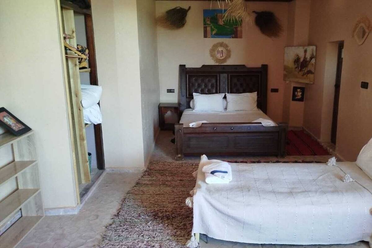 A bedroom with a large bed, a smaller bed, a nightstand, a dresser, and a door leading to another room.