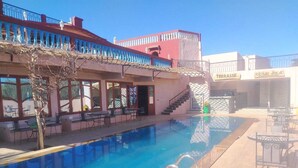 A swimming pool with a clear blue water, surrounded by outdoor seating and a staircase leading to an upper level. - Amlal Kasbah (Souk Lakhmis Dades)
