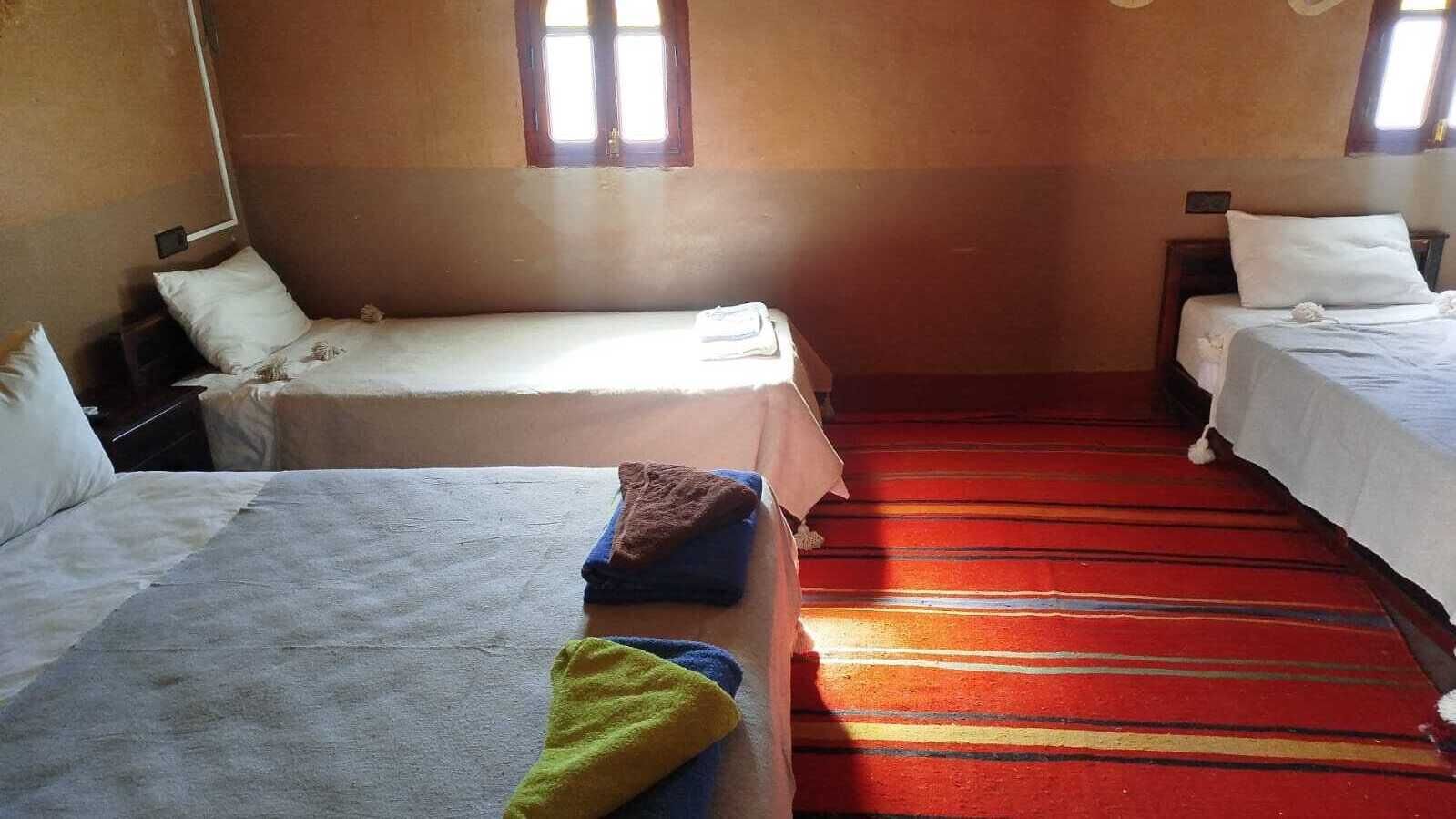 Una habitaci ón con dos camas, un suelo de alfombra a rayas rojas y un ventanal que deja entrar luz natural.