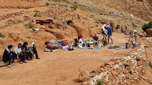 A group of people sitting and standing in a rocky outdoor area with a stream. - Amlal Kasbah (Souk Lakhmis Dades)