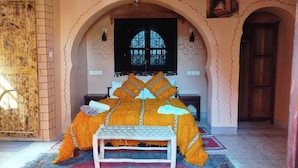 A room with a bed, a bench, and a window with a cross design. - Amlal Kasbah (Souk Lakhmis Dades)