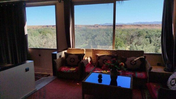 A living room with a sofa set, a coffee table, and a view of a mountainous landscape through large windows. - Amlal Kasbah (Souk Lakhmis Dades)