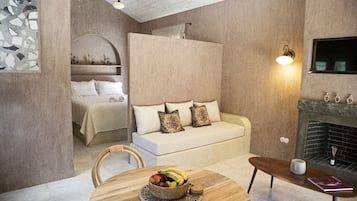 A cozy room with a bed, a sofa, a dining table with fruit, a fireplace, and a wall-mounted TV.