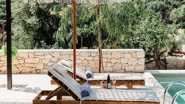A poolside area with two sun loungers, a stone wall, and a macrame umbrella. - Villa Nerithra, Private Pool and Garden, Furnished Terrace, Vathy, Ithaca (Ithaca)