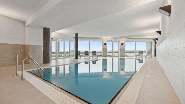 Ein großes Hallenbad mit freiem Blick auf die umliegende Landschaft, mit Fliesenboden und einer Metallleiter.