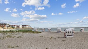 Ein Strand mit nummerierten Liegen und eine Reihe von Gebäuden im Hintergrund.