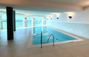 An indoor swimming pool with clear glass walls, a tiled floor, and a view of the sea. - Amazing apartment in OstseeOlpenitz with sauna (OstseeOlpenitz)