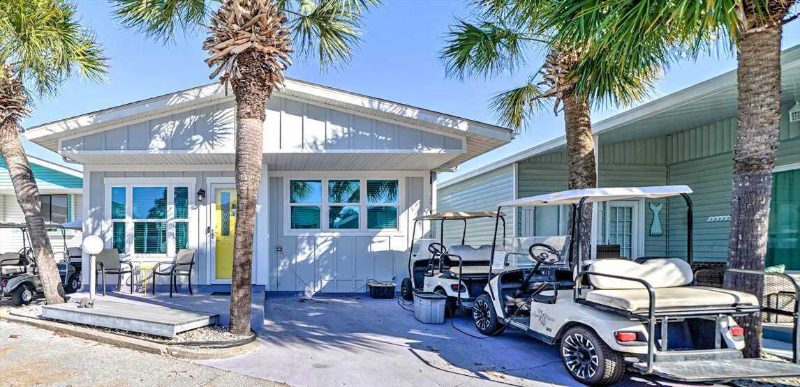 A two-story building with a white exterior, a covered patio area with chairs, and a golf cart parked in front.