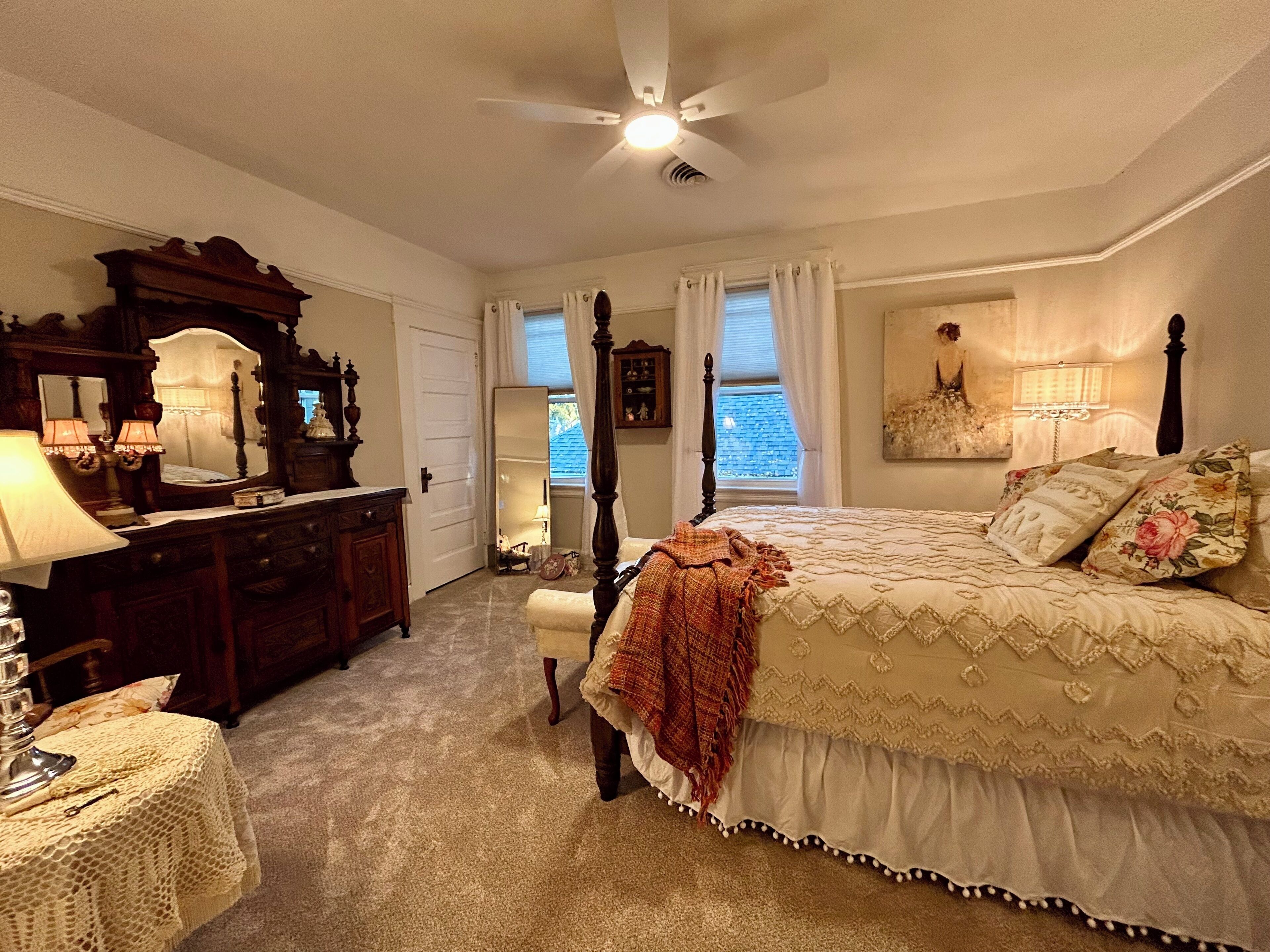 Une chambre à coucher avec un lit à baldaquin, une commode, un miroir et un ventilateur de plafond.