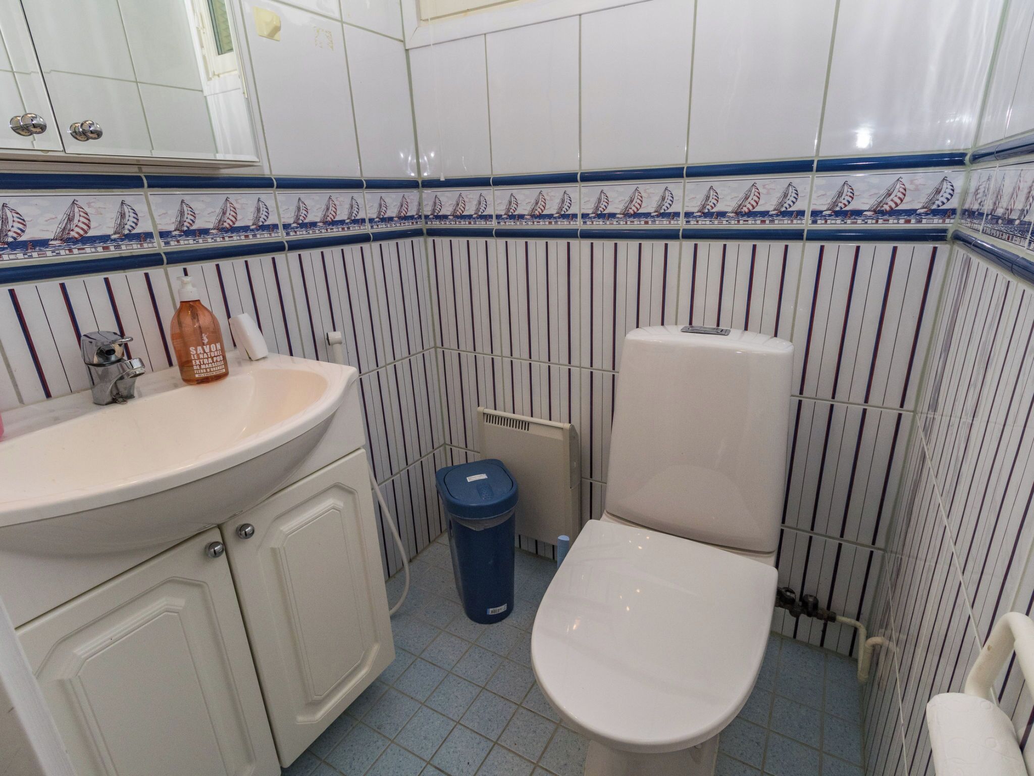 A bathroom with a white sink, a toilet, and a blue trash bin.