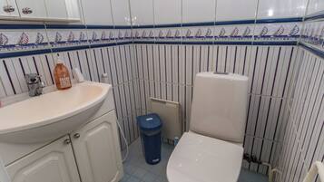 A bathroom with a white sink, a toilet, and a blue trash bin.