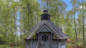 A small, rustic cabin with a hexagonal window and a chimney, surrounded by a forest.