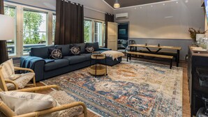 A spacious living room with a blue sofa, a wooden dining table, and a patterned rug.