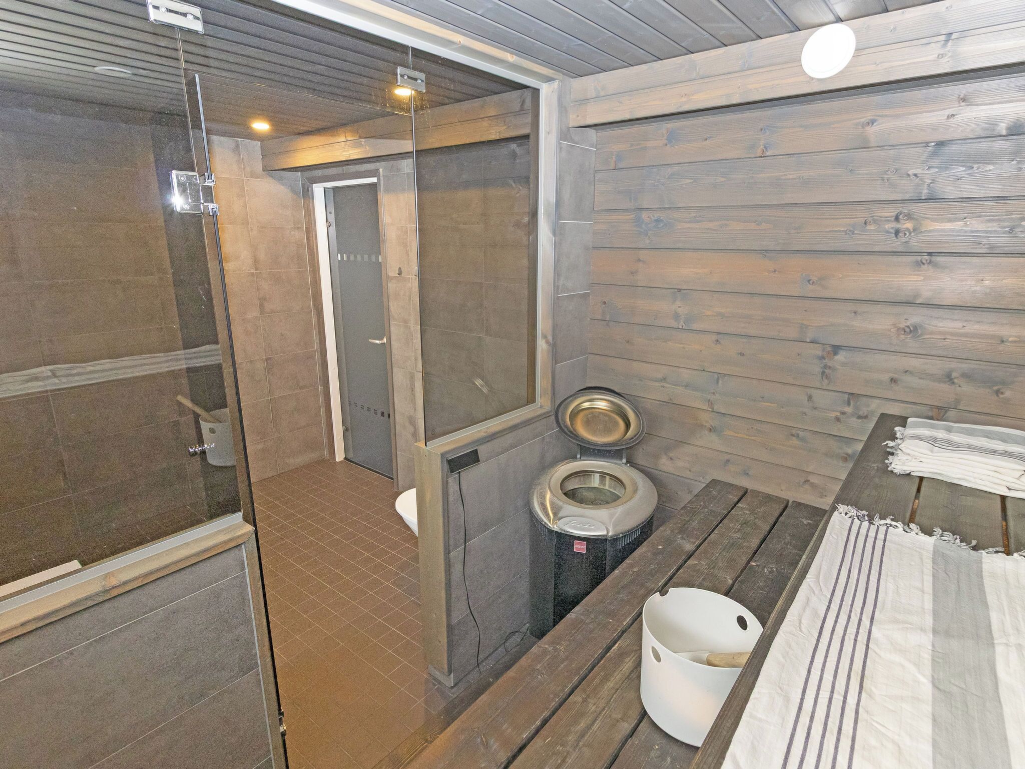 A sauna room with a wooden floor, a glass-enclosed shower area, and a toilet.