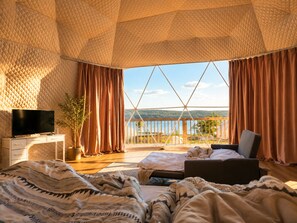 Een slaapkamer met een groot raam, een bed, een televisie en een houten bureau.