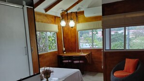 A compact room with a bed, a desk, and a chair. There are windows providing natural light and a view of the outside. - Nature, calm and comfort in a chalet close to everything but far from noise. (Guayaquil)