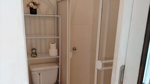 A compact bathroom with a toilet, a shower enclosure, and a shelf with toiletries. - Nature, calm and comfort in a chalet close to everything but far from noise. (Guayaquil)