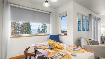 A dining area with a table set for two, a blue chair, and a view of the sea.