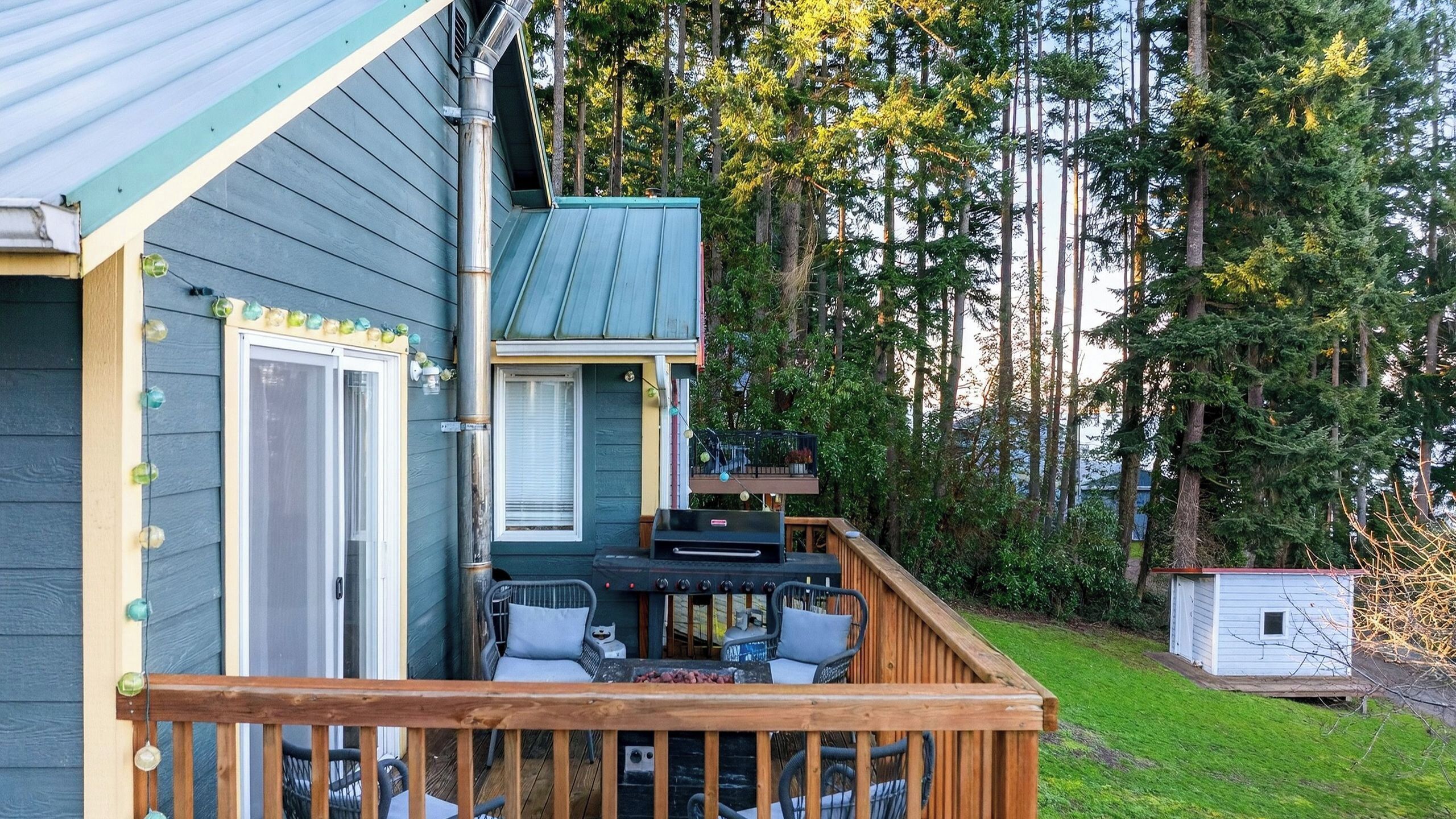 Une maison avec une terrasse, un barbecue et un petit abri de jardin.