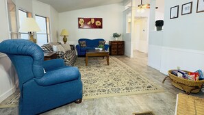 A spacious living room with a blue armchair, a sofa, a patterned rug, and a dining area with a table and chairs. - Restful, 2b/1b Unit along the Gasconade River (Richland)