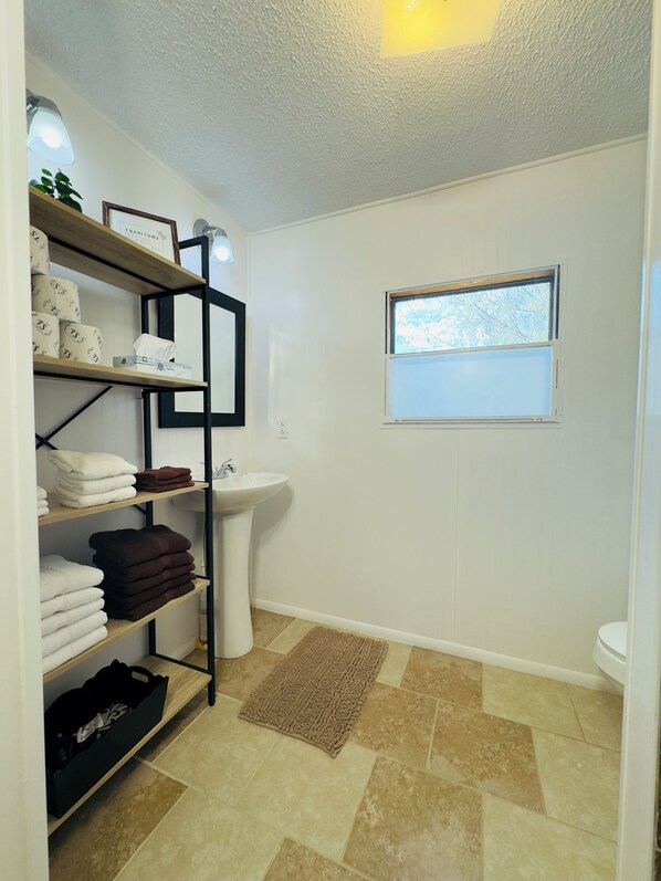 A bathroom with a white sink, a window, and shelves with towels and toiletries. - Restful, 2b/1b Unit along the Gasconade River (Richland)