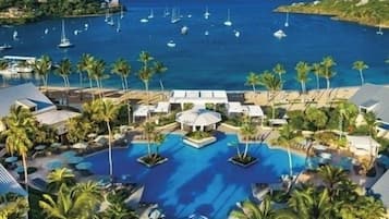 A resort with a large pool surrounded by palm trees and lounge chairs, overlooking a marina with boats.