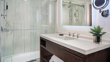 A modern bathroom with a glass shower enclosure, a white sink with two faucets, and a mirror with a round light.