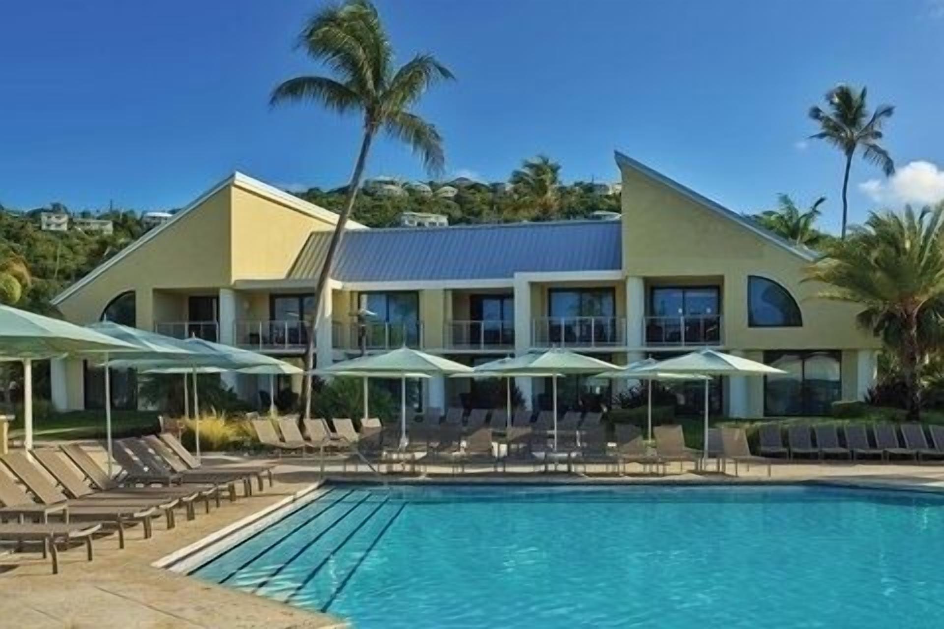 A hotel with a swimming pool, sun loungers, and umbrellas.