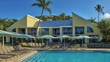 A hotel with a swimming pool, sun loungers, and umbrellas.