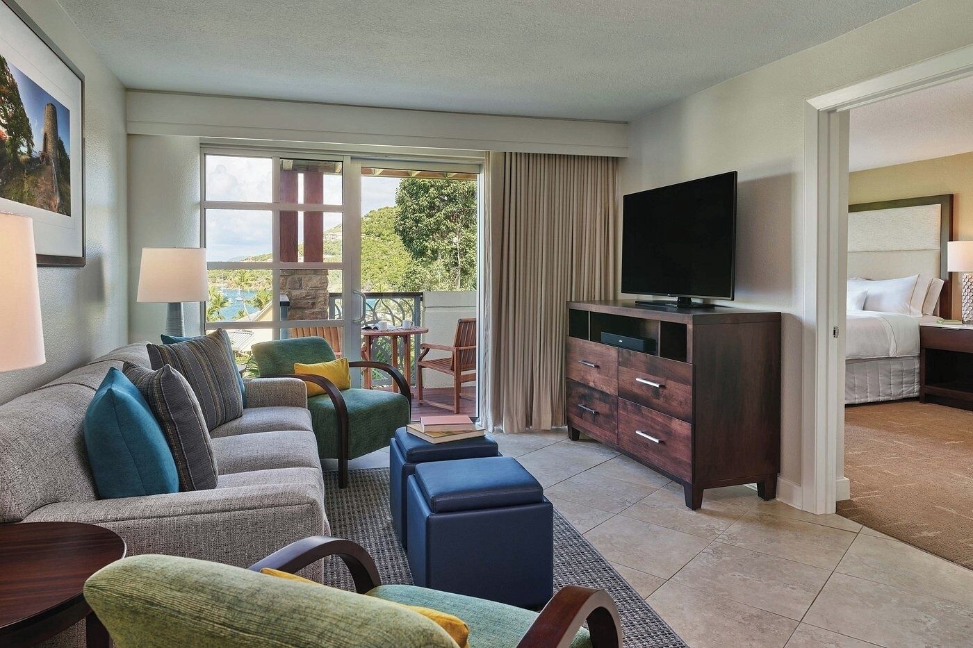 A hotel room with a sofa, chairs, a TV, a bed, and a balcony with a view.